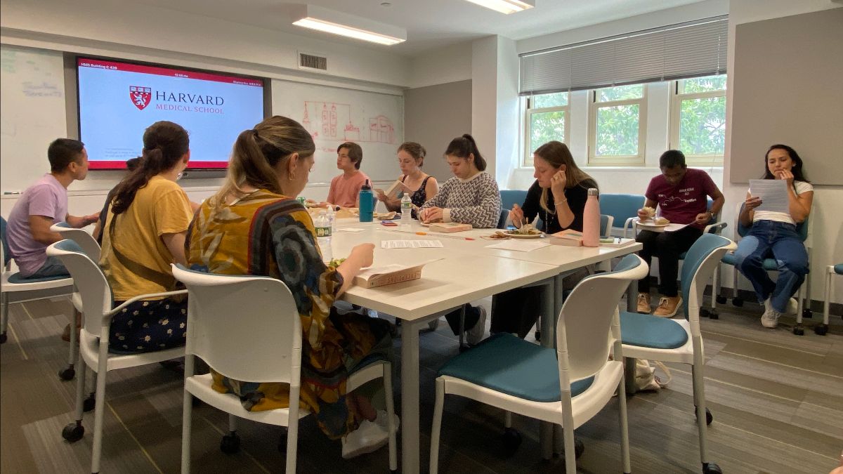 A group of people sitting at a conference table and around the room. 