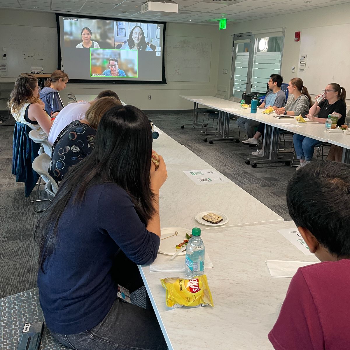 A group of people sitting at a conference table watching a Zoom screen. 